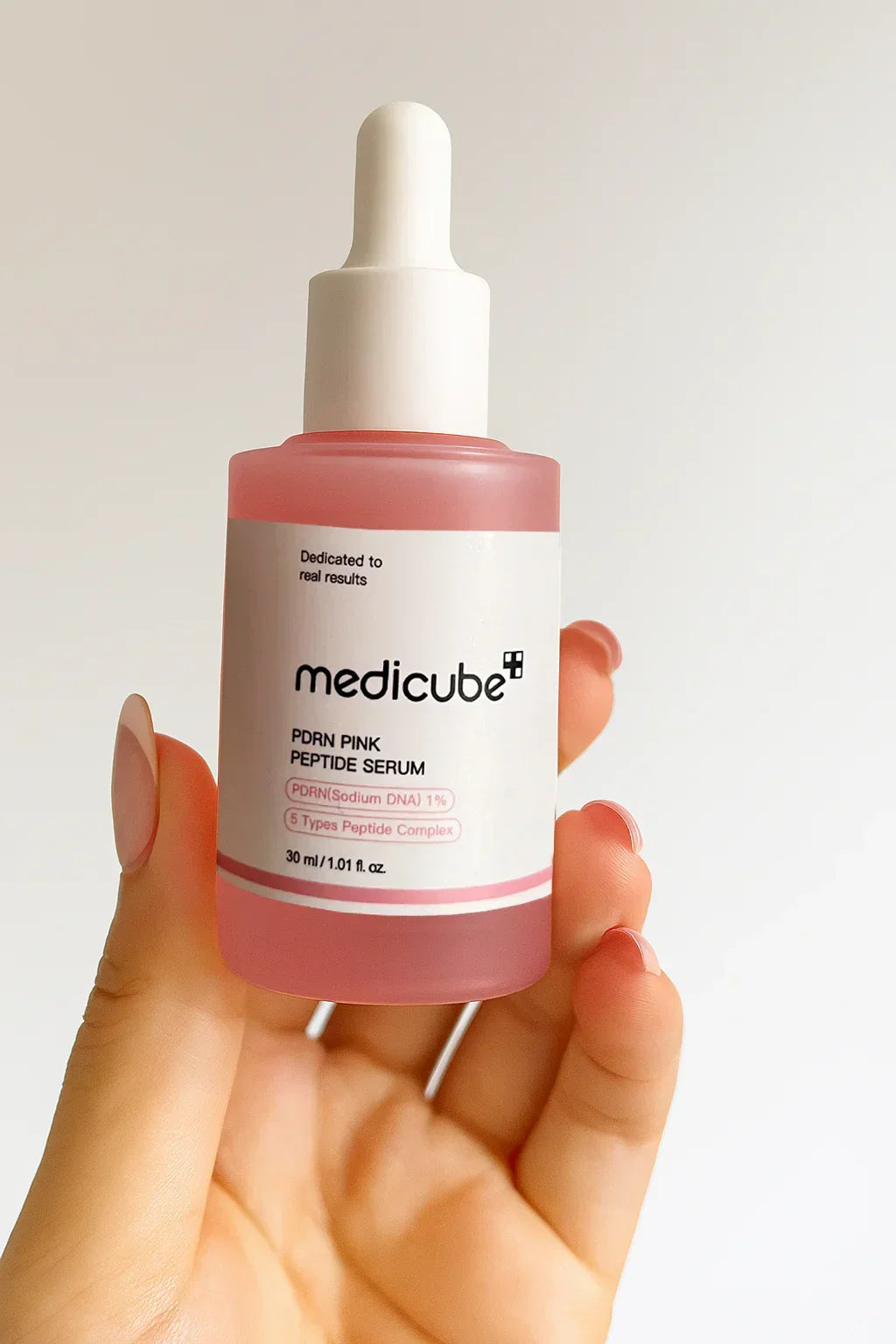 hand holding a bottle of medicube serum against a plain background