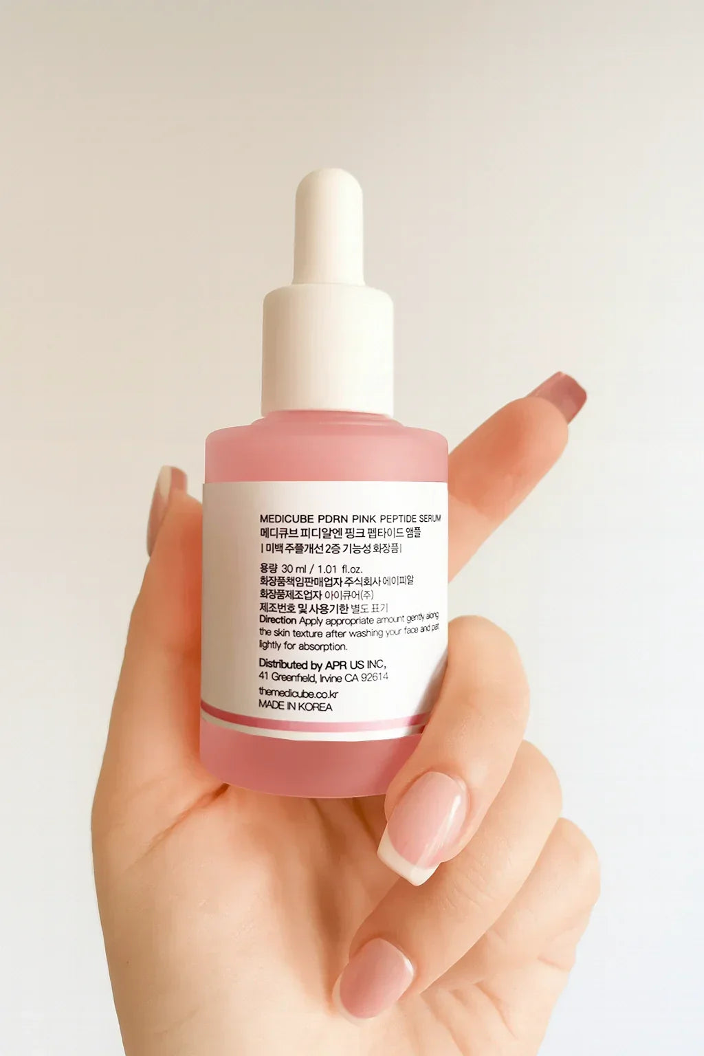 hand holding a pink skincare serum bottle with a white cap against a light background